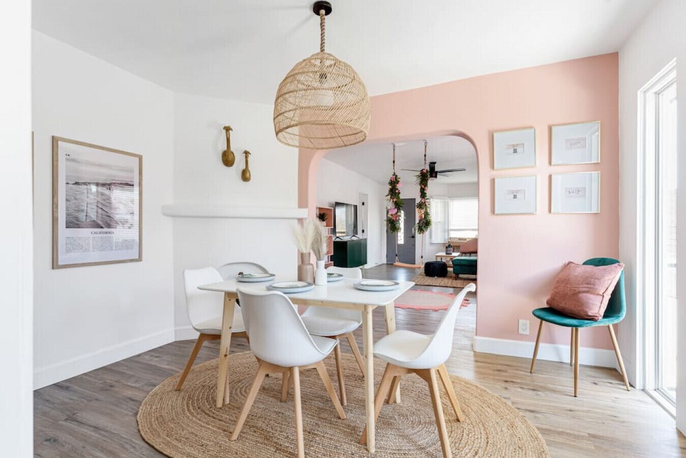Un'area pranzo moderna con un tavolo rotondo in legno, sedie bianche e una lampada a sospensione intrecciata.