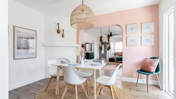 Un'area pranzo moderna con un tavolo rotondo in legno, sedie bianche e una lampada a sospensione intrecciata.