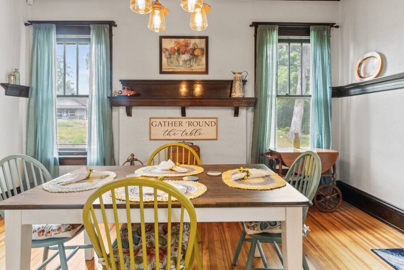A dining room with a wooden table, yellow chairs, and a 'GATHER 'ROUND the table' sign.