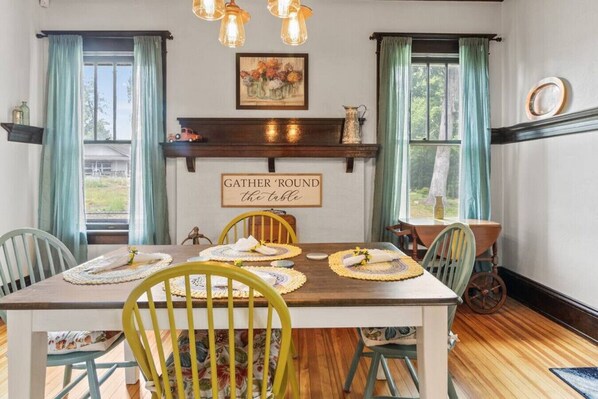 A dining room with a wooden table, yellow chairs, and a 'GATHER 'ROUND the table' sign.