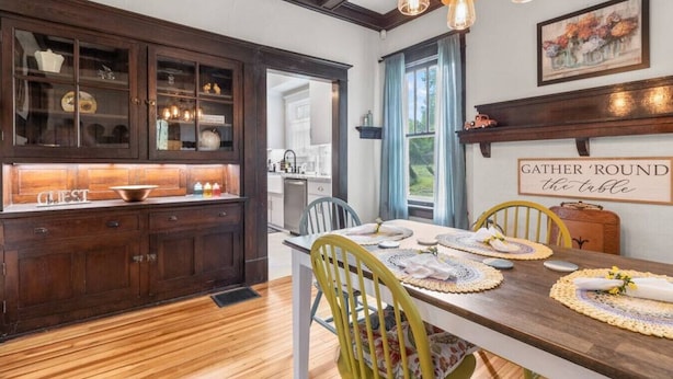 A dining area with a wooden table set for four, surrounded by dark wooden cabinets and a kitchen in the background. - Downtown Executive Retreat (Hickory)