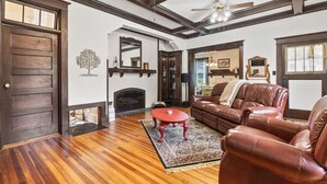 A spacious living room with hardwood flooring, a fireplace, leather furniture, and a ceiling fan. - Downtown Executive Retreat (Hickory)