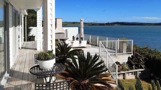 A balcony with a view of a lake, outdoor furniture, and a barbecue area. - Beachfront Luxury  (Clarks Beach)