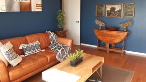 A living room with a brown leather sofa, a wooden coffee table, and a blue accent wall. - Beachfront Luxury  (Clarks Beach)