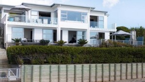 A modern two-story house with a balcony, large windows, and a well-maintained garden. - Beachfront Luxury  (Clarks Beach)