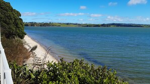 A coastal landscape with a sandy beach, clear blue water, and green hills in the distance. - Beachfront Luxury  (Clarks Beach)
