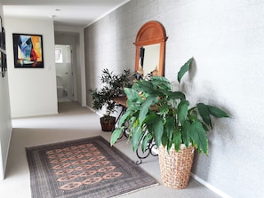 Un couloir avec un grand présentoir à plantes en osier, un miroir et un tapis à motifs.