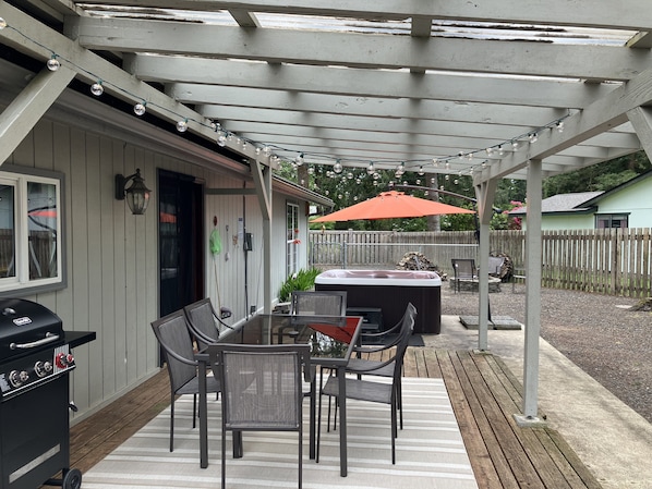 A covered patio with a grill, outdoor seating, and a hot tub.