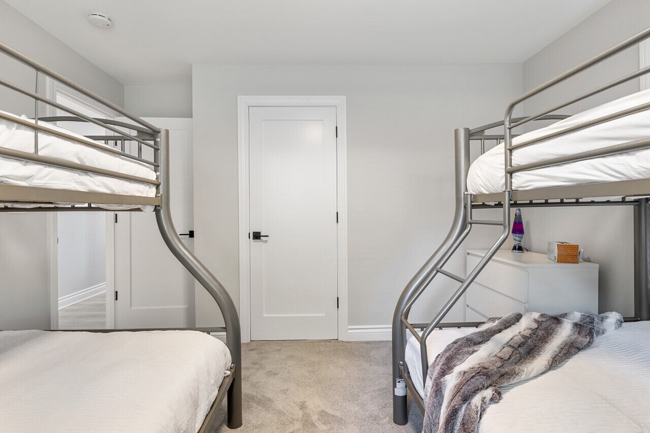 Ein Zimmer mit Etagenbetten, einer weißen Tür, einem kleinen Nachttisch mit Lampe und einer Decke auf dem Boden.