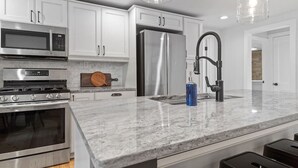 A modern kitchen with stainless steel appliances, white cabinetry, and a marble countertop. - Little Italy- Hilltop Cottage (Custer)