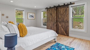 A bedroom with a bed, a large window, a sliding barn door, and a view of the outdoors. - Little Italy- Hilltop Cottage (Custer)