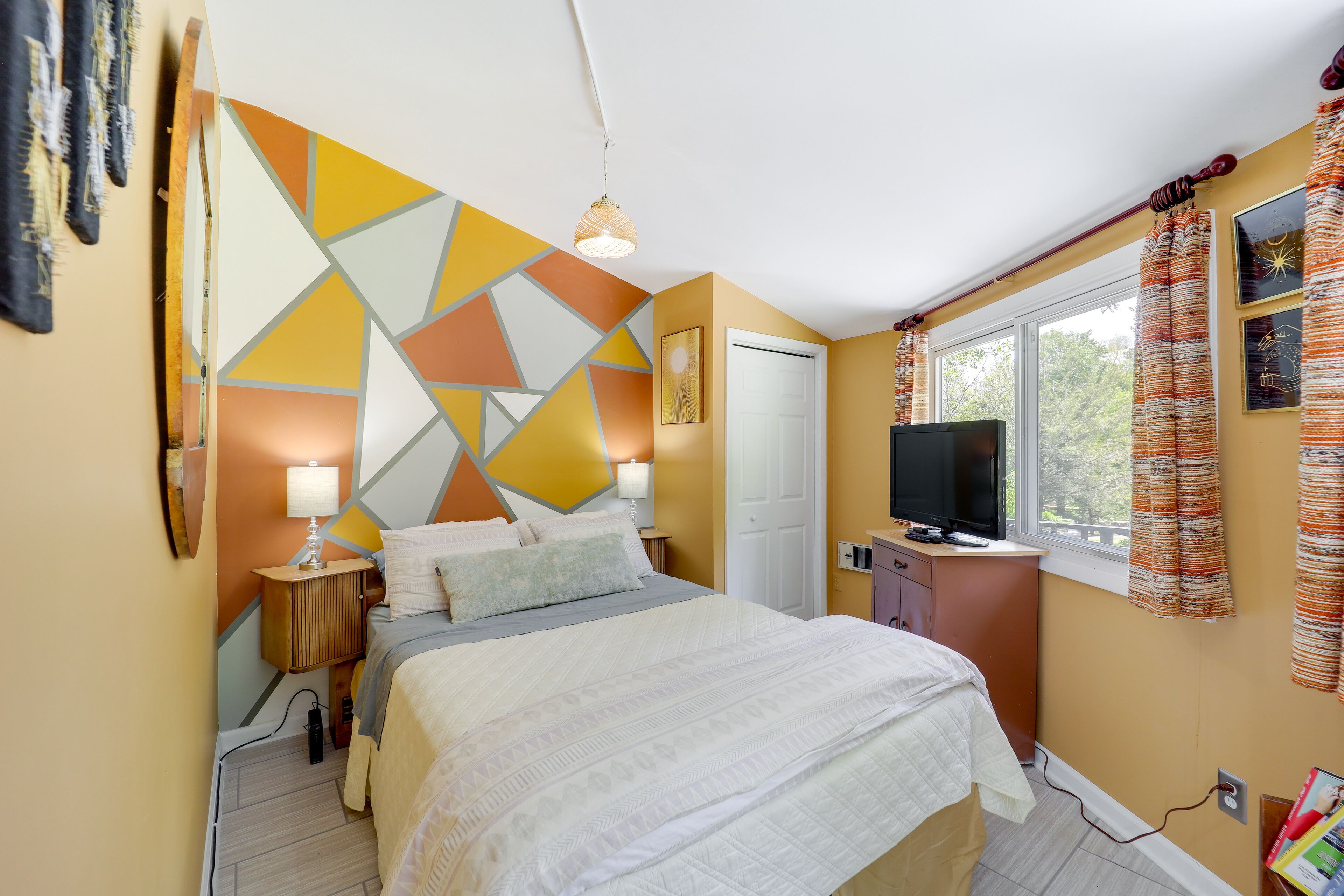 Een slaapkamer met een bed, een televisie, een raam met gordijnen en een geometrisch wandontwerp.