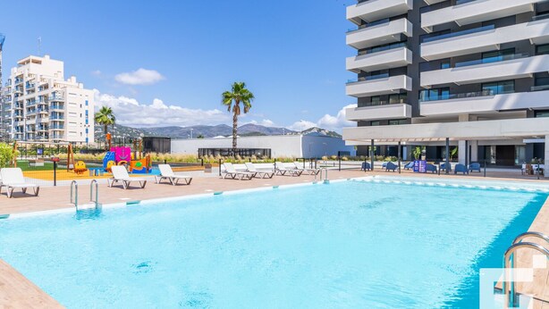 A swimming pool with lounge chairs, a children's play area, and modern buildings in the background. - Alexia II 123 - Grupo Turis - Calpe, Costa Blanca (Calpe)