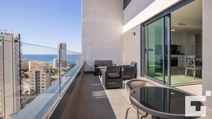 A balcony with a glass door leading to a kitchen, a dining area with chairs, and a view of the sea and buildings. - Alexia II 123 - Grupo Turis - Calpe, Costa Blanca (Calpe)