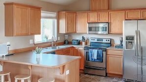 Una cocina moderna con armarios de madera, una isla central con taburetes, electrodomésticos de acero inoxidable y suelo de baldosas.