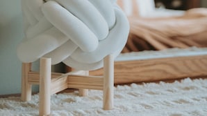Una escultura blanca y abstracta sobre un pedestal de madera en una habitación con una cama y un armario de madera al fondo.