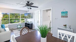 A modern living room with a dining table, chairs, a ceiling fan, a TV, and a view of the outdoors. - 4 Unique Cottages Sleeps 16 Comfortably on 1 Acre (Coloma)