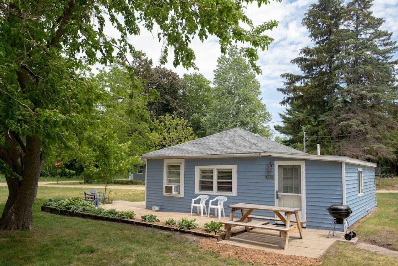A small blue house with a front porch, a picnic table, and a barbecue grill.