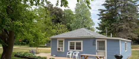 A small blue house with a front porch, a picnic table, and a barbecue grill.