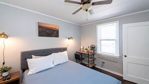 A bedroom with a bed, a desk, a ceiling fan, a window, and a door. - 4 Unique Cottages Sleeps 16 Comfortably on 1 Acre (Coloma)