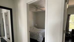 Quarto com cama, ventilador de teto e porta para outro cômodo.