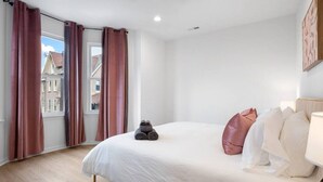 Ein Schlafzimmer mit Bett, Kissen, einer Lampe und einem Fenster mit Vorhängen.