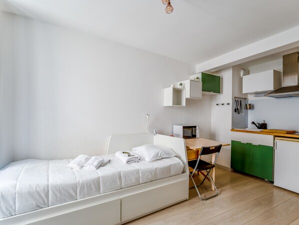 A compact room with a bed, a small desk, and a kitchenette. - Studio Zielon - Welkeys (Avignon)