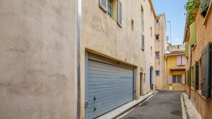 Uma rua estreita com edifícios em ambos os lados, apresentando uma porta de garagem fechada e uma pequena porta à direita.