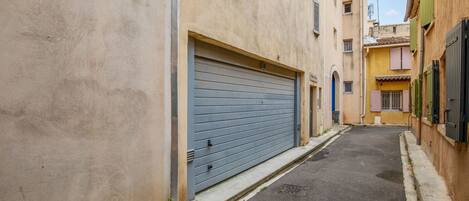 Une rue étroite, bordée de bâtiments des deux côtés, avec une porte de garage fermée et une petite porte sur la droite.