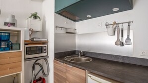 Uma cozinha compacta com micro-ondas, torradeira e cafeteira em uma estante branca. Uma pia e uma máquina de lavar louça estão embutidas nos armários.