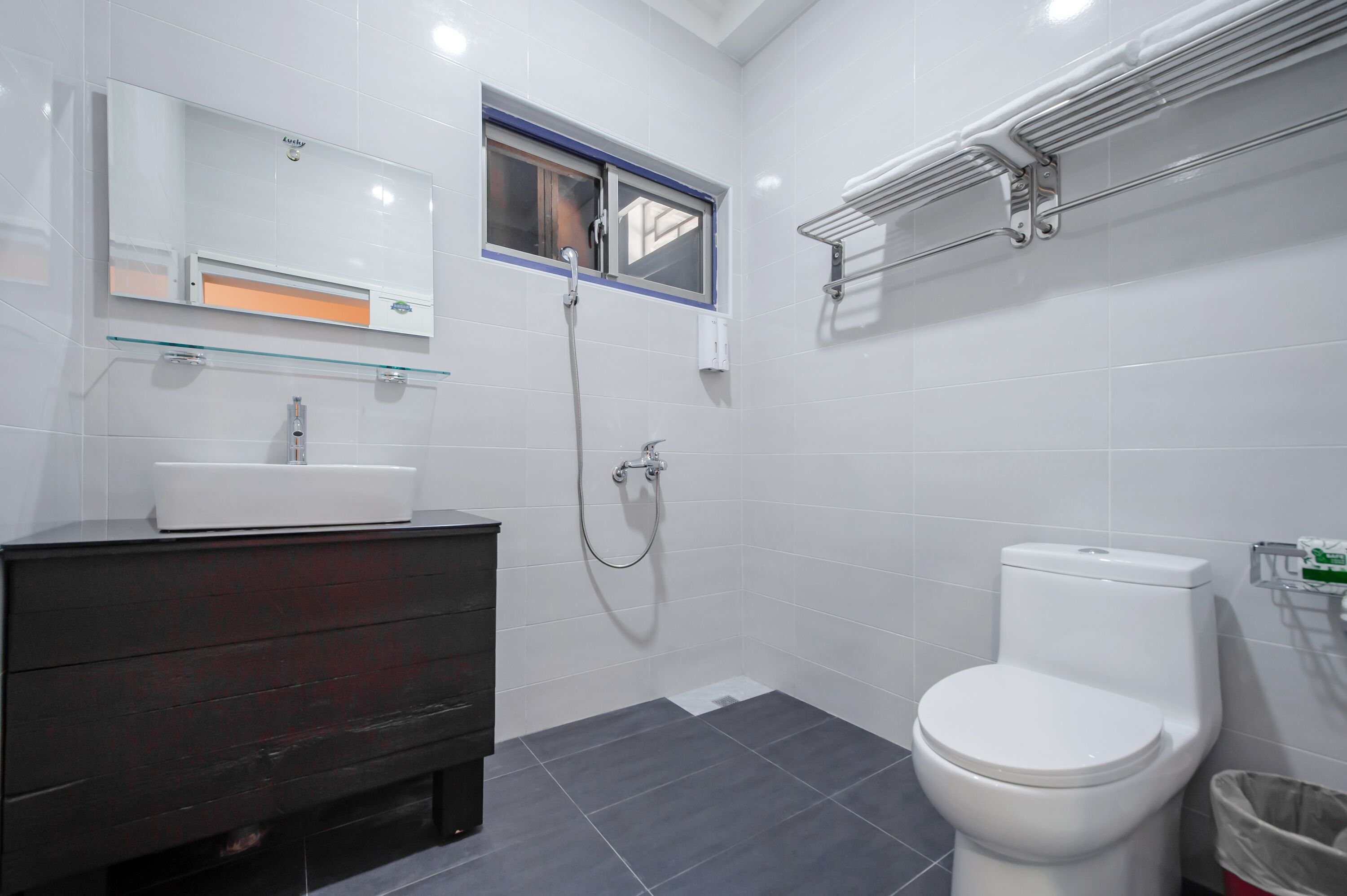 Un baño moderno con inodoro blanco, repisa de vidrio sobre el lavamanos y ventana sobre la ducha.