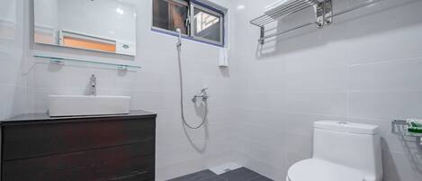 Un baño moderno con inodoro blanco, repisa de vidrio sobre el lavamanos y ventana sobre la ducha.