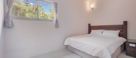 A bedroom with a bed, a nightstand, a window with curtains, and a wall-mounted light.