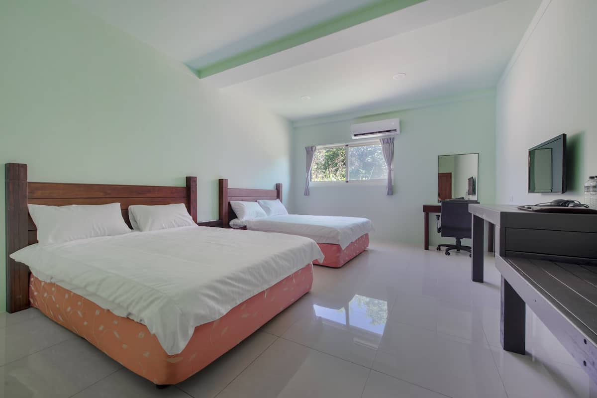 A hotel room with two beds, a desk, a chair, an air conditioning unit, and a television.