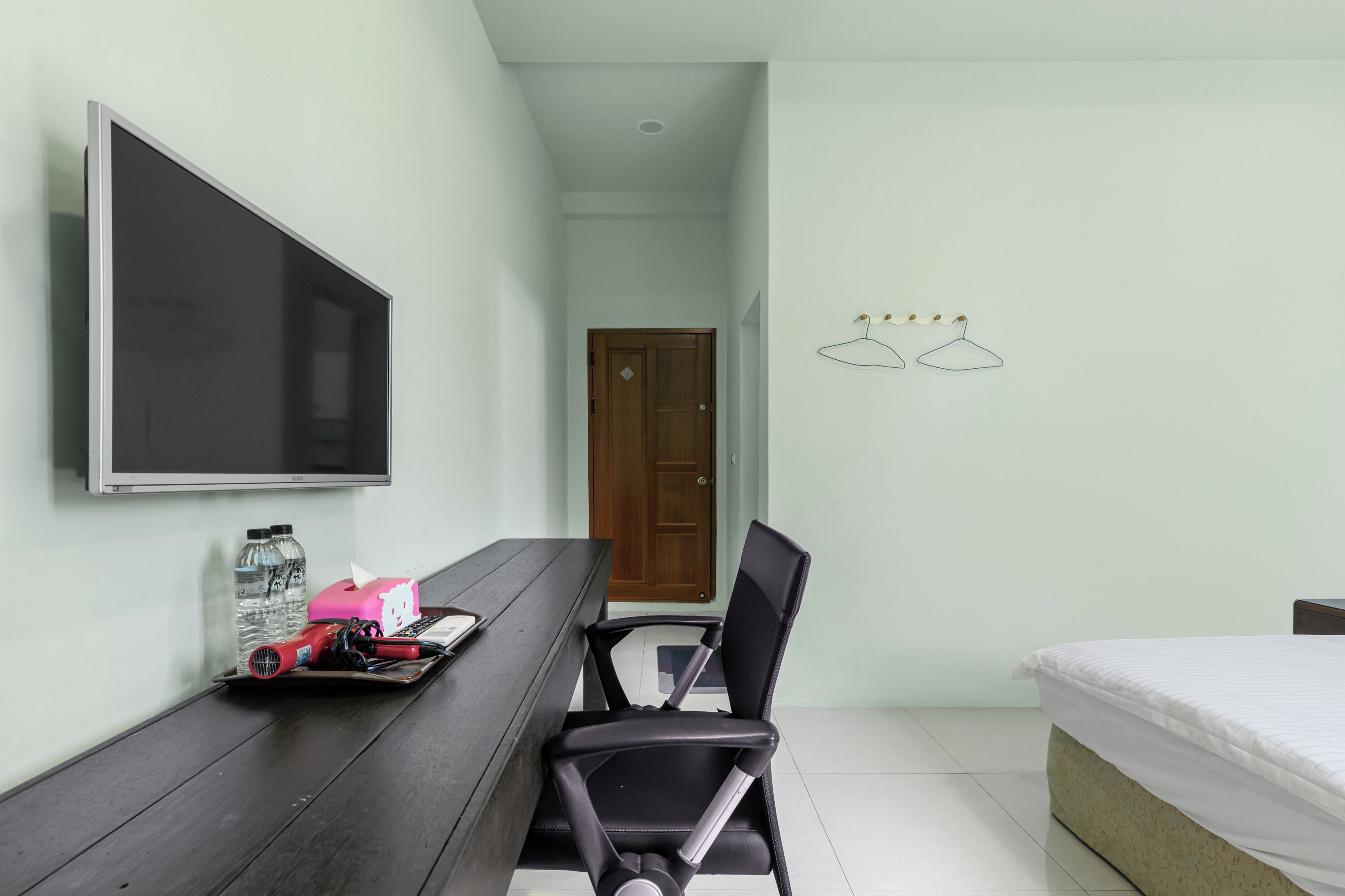 A small, clean room with a bed, a desk with a chair, a TV, and a door.