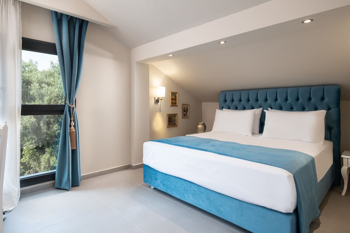 A bedroom with a large bed, a window with curtains, a bedside table, and a wall-mounted lamp.