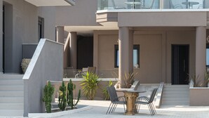 A modern two-story house with a balcony, outdoor seating, and a patio area with plants. - MYKONIATIKA VILLAS (Nea Propontida)