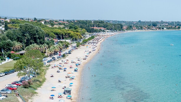 A coastal beach with rows of beach umbrellas and sun loungers, a clear blue sea, and a parking area with cars. - MYKONIATIKA VILLAS (Nea Propontida)