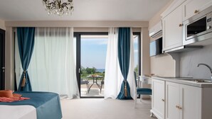 A hotel room with a bed, a kitchenette, a dining area with a table and chairs, and a view of the outdoors. - MYKONIATIKA VILLAS (Nea Propontida)