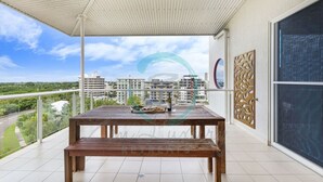 A balcony with a wooden table and bench, a decorative wall panel, and a view of a cityscape. - ZEN LUXURY 2-STORY Penthouse Mindal View (Darwin)