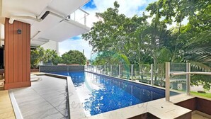 Una piscina con barrera de vidrio, rodeada de exuberante follaje y un diseño arquitectónico moderno.