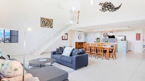 Amplia sala de estar con sofá, reposapiés y mesa de comedor. Una escalera conduce a un nivel superior.