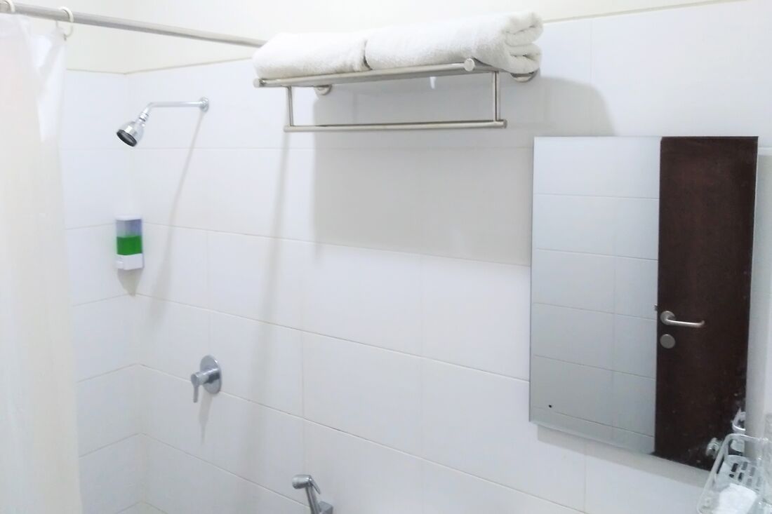 A bathroom with white tiled walls, a shower with a handheld showerhead, a towel rack, a soap dispenser, and a mirror with a door.