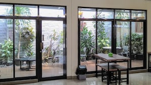 Un espacio interior amplio con grandes puertas correderas de vidrio que dan a un jardín. Hay varias mesas y sillas dispuestas para comer o socializar.