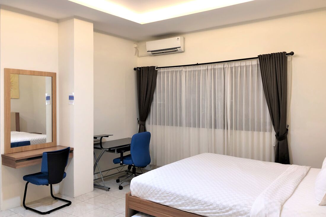 A hotel room with a bed, a desk with a chair, a mirror, and a window with curtains.