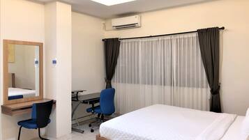 A hotel room with a bed, a desk with a chair, a mirror, and a window with curtains.