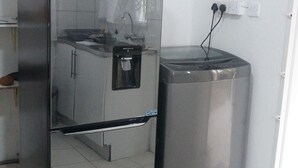 Kompakti keittiö, jossa on ruostumattomasta teräksestä valmistettu jääkaappi, vesihana ja roskakori.