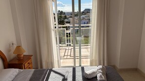 Une chambre à coucher avec un lit, une table de chevet avec une lampe et une vue sur un balcon doté d’une balustrade.
