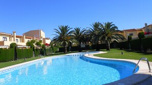 Une piscine à l’eau d’un bleu cristallin, entourée de pelouse bien entretenue et de palmiers.