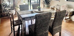 A dining area with a wooden table, woven chairs, and potted plants.